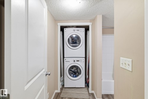 Laundry area featuring a textured ceiling, stacked washing machine and dryer, and wood finished floors - 424 1510 Watt Drive, Edmonton, AB - Indoor Photo Showing Laundry Room
