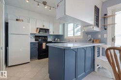 Kitchen featuring open shelves, two tone cabinetry, freestanding refrigerator, a peninsula, and black range with electric cooktop - 
