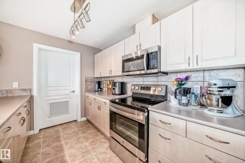 Kitchen with stainless steel appliances, light countertops, light tile patterned floors, backsplash, and rail lighting - 232 530 Hooke Road, Edmonton, AB - Indoor Photo Showing Kitchen