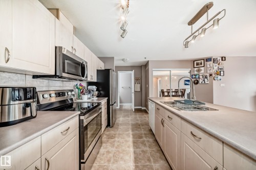 Kitchen featuring stainless steel appliances, light countertops, tasteful backsplash, and light tile patterned flooring - 232 530 Hooke Road, Edmonton, AB - Indoor Photo Showing Kitchen With Upgraded Kitchen