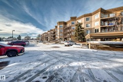Snow covered property featuring a view of apartment building / complex and covered and uncovered parking - 