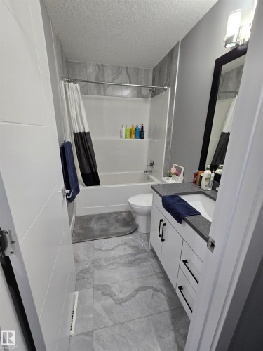 Bathroom with vanity, shower / bath combo, a textured ceiling, and light marble finish flooring - 1641 Enright Way Nw, Edmonton, AB - Indoor Photo Showing Bathroom