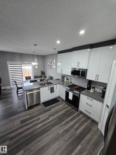 Kitchen with a peninsula, white cabinetry, a textured ceiling, stainless steel appliances, and hanging light fixtures - 1641 Enright Way Nw, Edmonton, AB - Indoor Photo Showing Kitchen With Double Sink