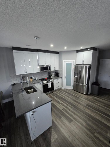 Kitchen with white cabinetry, a peninsula, stainless steel appliances, dark stone counters, and a textured ceiling - 1641 Enright Way Nw, Edmonton, AB - Indoor Photo Showing Kitchen With Double Sink