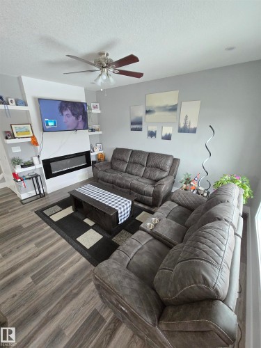Living room with a glass covered fireplace, a textured ceiling, ceiling fan, and wood finished floors - 1641 Enright Way Nw, Edmonton, AB - Indoor Photo Showing Living Room