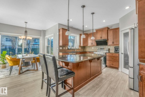 Kitchen with a kitchen breakfast bar, brown cabinets, pendant lighting, a chandelier, and stainless steel appliances - 2307 Rutherford Way, Edmonton, AB - Indoor