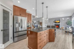 Kitchen with brown cabinets, stainless steel fridge, a kitchen island, pendant lighting, and light wood-style flooring - 