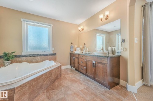 Full bath featuring double vanity, a jetted tub, healthy amount of natural light, and light tile patterned floors - 2307 Rutherford Way, Edmonton, AB - Indoor Photo Showing Bathroom