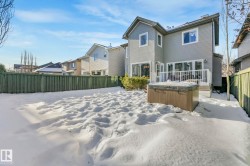 Snow covered rear of property with a hot tub, a fenced backyard, and a wooden deck - 
