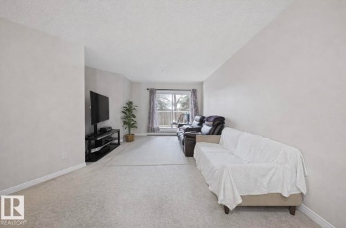 Living room featuring light carpet and a textured ceiling - 103 12110 119 Ave, Edmonton, AB - Indoor