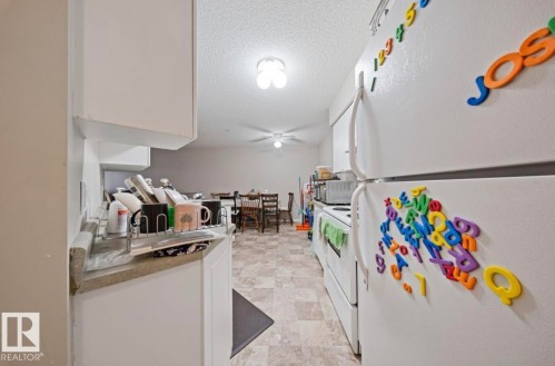 Kitchen with white appliances, white cabinetry, a textured ceiling, light countertops, and ceiling fan - 103 12110 119 Ave, Edmonton, AB - Indoor Photo Showing Other Room