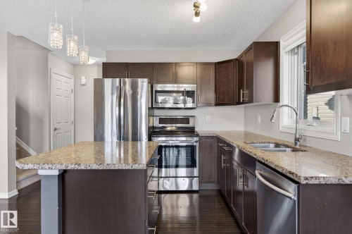 Kitchen with dark wood finish cabinets, stainless steel appliances, light stone countertops, and a textured ceiling - 2338 Casselman Crescent, Edmonton, AB - Indoor Photo Showing Kitchen With Stainless Steel Kitchen With Double Sink With Upgraded Kitchen