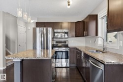 Kitchen with dark wood finish cabinets, stainless steel appliances, light stone countertops, and a textured ceiling - 
