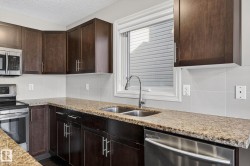 Kitchen featuring stainless steel appliances, light stone counters, dark wood finish cabinetry, and a textured ceiling - 
