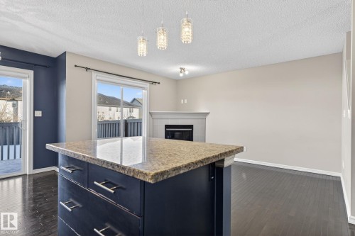 Kitchen featuring pendant lighting, light stone counters, dark wood finished floors, a tiled fireplace, and a textured ceiling - 2338 Casselman Crescent, Edmonton, AB - Indoor Photo Showing Kitchen