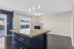 Kitchen featuring pendant lighting, light stone counters, dark wood finished floors, a tiled fireplace, and a textured ceiling - 