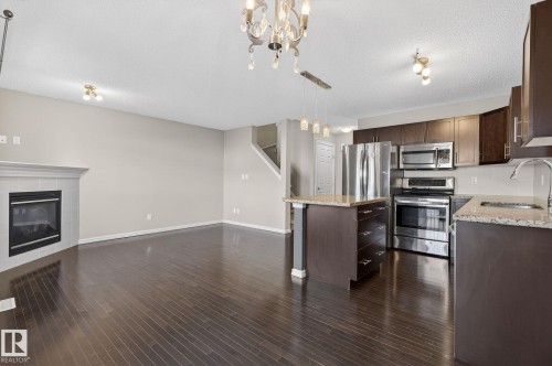 Kitchen featuring dark wood finish cabinets, stainless steel appliances, light stone countertops, open floor plan, and a textured ceiling - 2338 Casselman Crescent, Edmonton, AB - Indoor Photo Showing Kitchen With Stainless Steel Kitchen