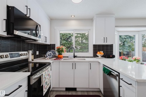 Kitchen with stainless steel appliances, white cabinets, a peninsula, healthy amount of natural light, and a textured ceiling - 10423 35 Avenue, Edmonton, AB - Indoor Photo Showing Kitchen