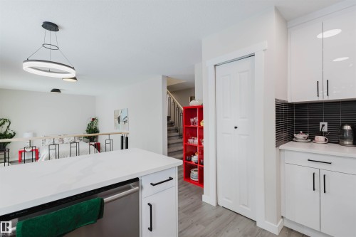 Kitchen with white cabinets, dishwasher, light wood finished floors, hanging light fixtures, and light stone counters - 10423 35 Avenue, Edmonton, AB - Indoor Photo Showing Kitchen