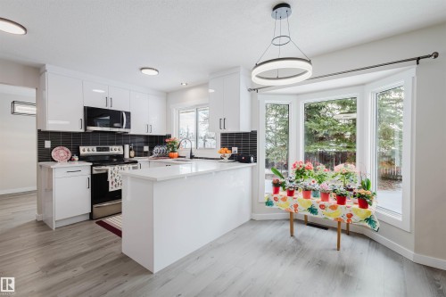 Kitchen with stainless steel appliances, a peninsula, white cabinetry, hanging light fixtures, and decorative backsplash - 10423 35 Avenue, Edmonton, AB - Indoor Photo Showing Kitchen