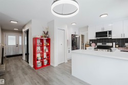 Kitchen with stainless steel appliances, white cabinets, a peninsula, light wood-type flooring, and decorative backsplash - 