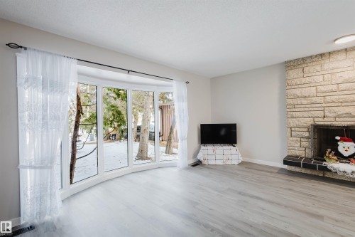 Unfurnished living room with a stone fireplace and wood finished floors - 10423 35 Avenue, Edmonton, AB - Indoor Photo Showing Living Room With Fireplace