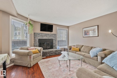 Living room with wood finished floors, a stone fireplace, and a textured ceiling - 3 1820 56 Street, Edmonton, AB - Indoor Photo Showing Living Room With Fireplace