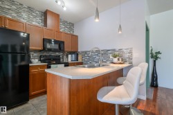 Kitchen featuring black appliances, tasteful backsplash, a breakfast bar, a peninsula, and light countertops - 