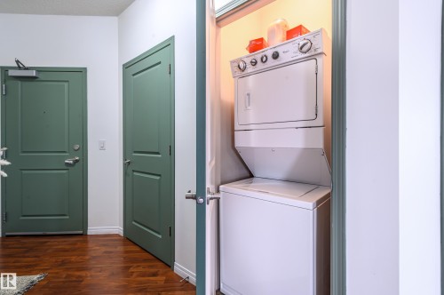 Laundry area with stacked washer and clothes dryer and dark wood-style floors - 411 1619 James Mowatt Trail, Edmonton, AB - Indoor Photo Showing Laundry Room