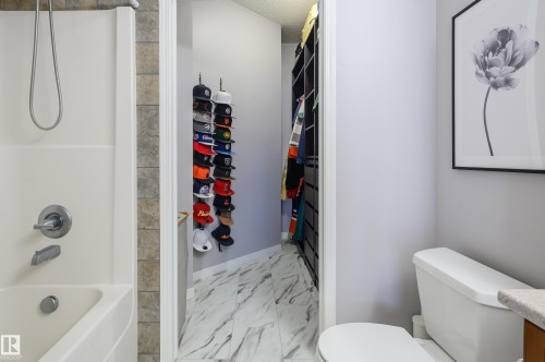 Full bathroom with vanity, shower / tub combination, light marble finish flooring, a textured ceiling, and a walk in closet - 411 1619 James Mowatt Trail, Edmonton, AB - Indoor Photo Showing Bathroom
