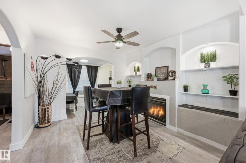Dining area with arched walkways, light wood-style floors, a glass covered fireplace, and ceiling fan - 10656 93 Street, Edmonton, AB - Indoor With Fireplace