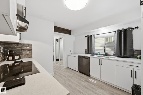 Kitchen featuring white cabinets, decorative backsplash, light wood-style floors, stainless steel dishwasher, and black electric cooktop - 10656 93 Street, Edmonton, AB - Indoor Photo Showing Kitchen