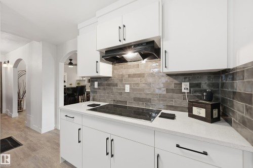 Kitchen with arched walkways, white cabinetry, black electric stovetop, light stone counters, and tasteful backsplash - 10656 93 Street, Edmonton, AB - Indoor Photo Showing Kitchen