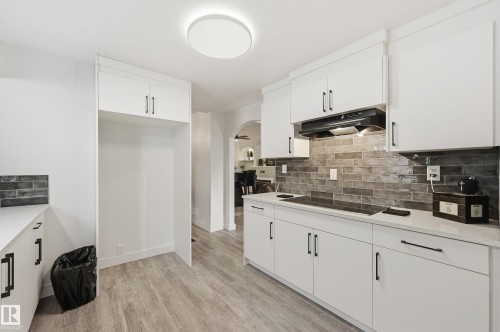 Kitchen featuring arched walkways, white cabinetry, backsplash, light wood-style flooring, and black electric cooktop - 10656 93 Street, Edmonton, AB - Indoor Photo Showing Kitchen