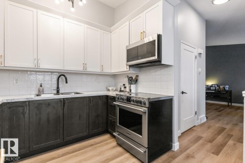 Kitchen featuring dual tone cabinetry, stainless steel appliances, light wood finished floors, and decorative backsplash - 6411 180 Street, Edmonton, AB - Indoor Photo Showing Kitchen With Double Sink With Upgraded Kitchen