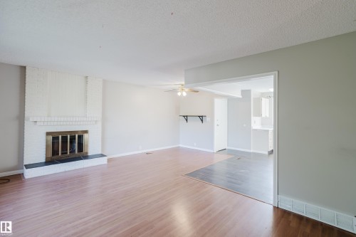 Unfurnished living room with a ceiling fan, a fireplace, light wood-type flooring, and a textured ceiling - Edmonton, AB - Indoor Photo Showing Living Room With Fireplace