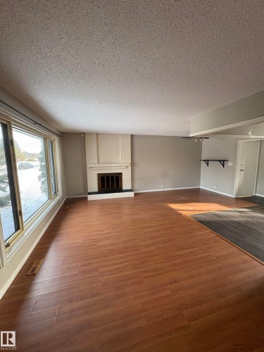 Unfurnished living room with a textured ceiling, dark wood-style flooring, and a brick fireplace - Edmonton, AB - Indoor Photo Showing Other Room
