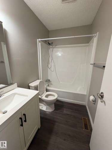 Bathroom featuring vanity, bathing tub / shower combination, dark wood finished floors, and a textured ceiling - Edmonton, AB - Indoor Photo Showing Bathroom