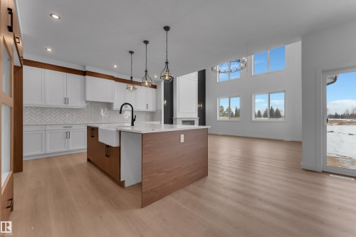 Dual tone kitchen featuring two tone cabinets, a center island with sink, light wood-style floors, open floor plan, and light stone countertops - 40 Grayson Green, Stony Plain, AB - Indoor Photo Showing Kitchen With Upgraded Kitchen
