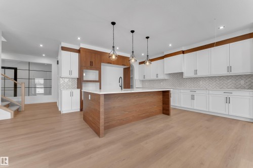 Kitchen with a center island with sink, pendant lighting, dual tone cabinetry, light stone countertops, and light wood-type flooring - 40 Grayson Green, Stony Plain, AB - Indoor Photo Showing Kitchen
