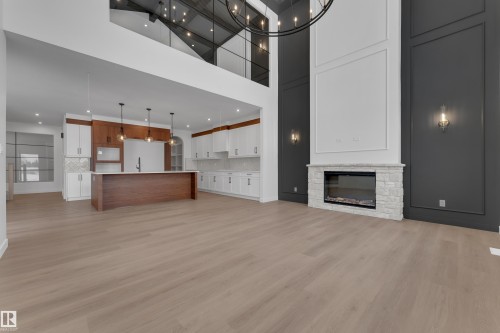 Unfurnished living room with light wood-style floors, a stone fireplace, a high ceiling, and suspended lighting - 40 Grayson Green, Stony Plain, AB - Indoor With Fireplace