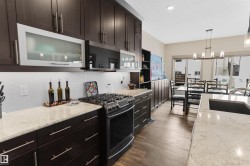 Kitchen featuring light stone countertops, gas stove, dark wood finish cabinetry, tasteful backsplash, and hanging lights - 