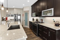 Kitchen with stainless steel appliances, light stone countertops, glass fronted cabinets, and hanging light fixtures - 