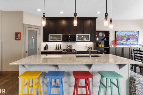 Kitchen featuring dark wood-style flooring, a center island with sink, pendant lighting, stainless steel appliances, and open shelves - 97 Astoria Point(E), Devon, AB - Indoor Photo Showing Kitchen With Upgraded Kitchen