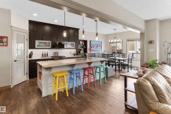Kitchen with a kitchen breakfast bar, light stone counters, dark wood-style floors, stainless steel appliances, and a kitchen island with sink - 