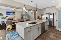 Kitchen featuring stainless steel appliances, a ceiling fan, a fireplace, decorative light fixtures, and light stone counters - 