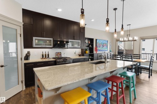 Kitchen with light stone counters, open shelves, dark wood-style flooring, a kitchen island with sink, and a kitchen bar - 97 Astoria Point(E), Devon, AB - Indoor Photo Showing Kitchen With Upgraded Kitchen