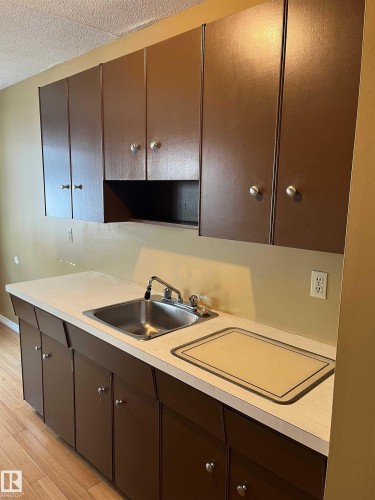 Kitchen featuring dark wood finish cabinets, light countertops, light wood-type flooring, and a textured ceiling - 203 8524 Gateway Boulevard, Edmonton, AB - Indoor Photo Showing Kitchen