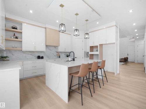 Kitchen with hanging light fixtures, a breakfast bar area, modern cabinets, open shelves, and light wood-style floors - 1168 Gyrfalcon Crescent, Edmonton, AB - Indoor Photo Showing Kitchen With Upgraded Kitchen