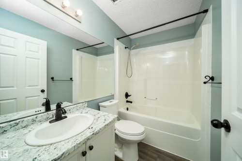 Bathroom featuring vanity, shower / bath combination, a textured ceiling, and dark wood finished floors - 1695 Tompkins Place, Edmonton, AB - Indoor Photo Showing Bathroom